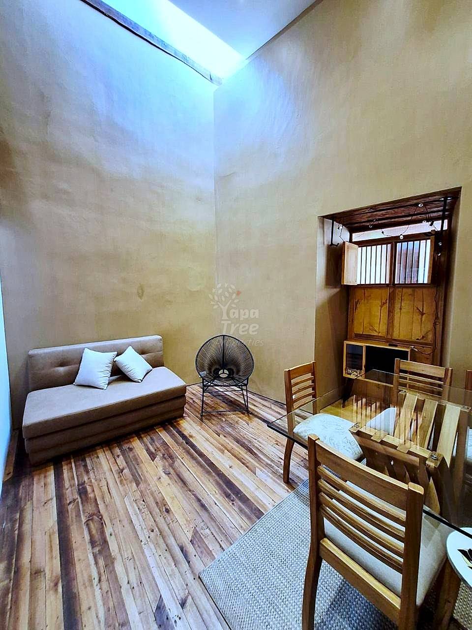 Living room with tan plaster walls, wooden flooring, beige sofa with pillows, black metal chair, and wooden furniture under skylight.