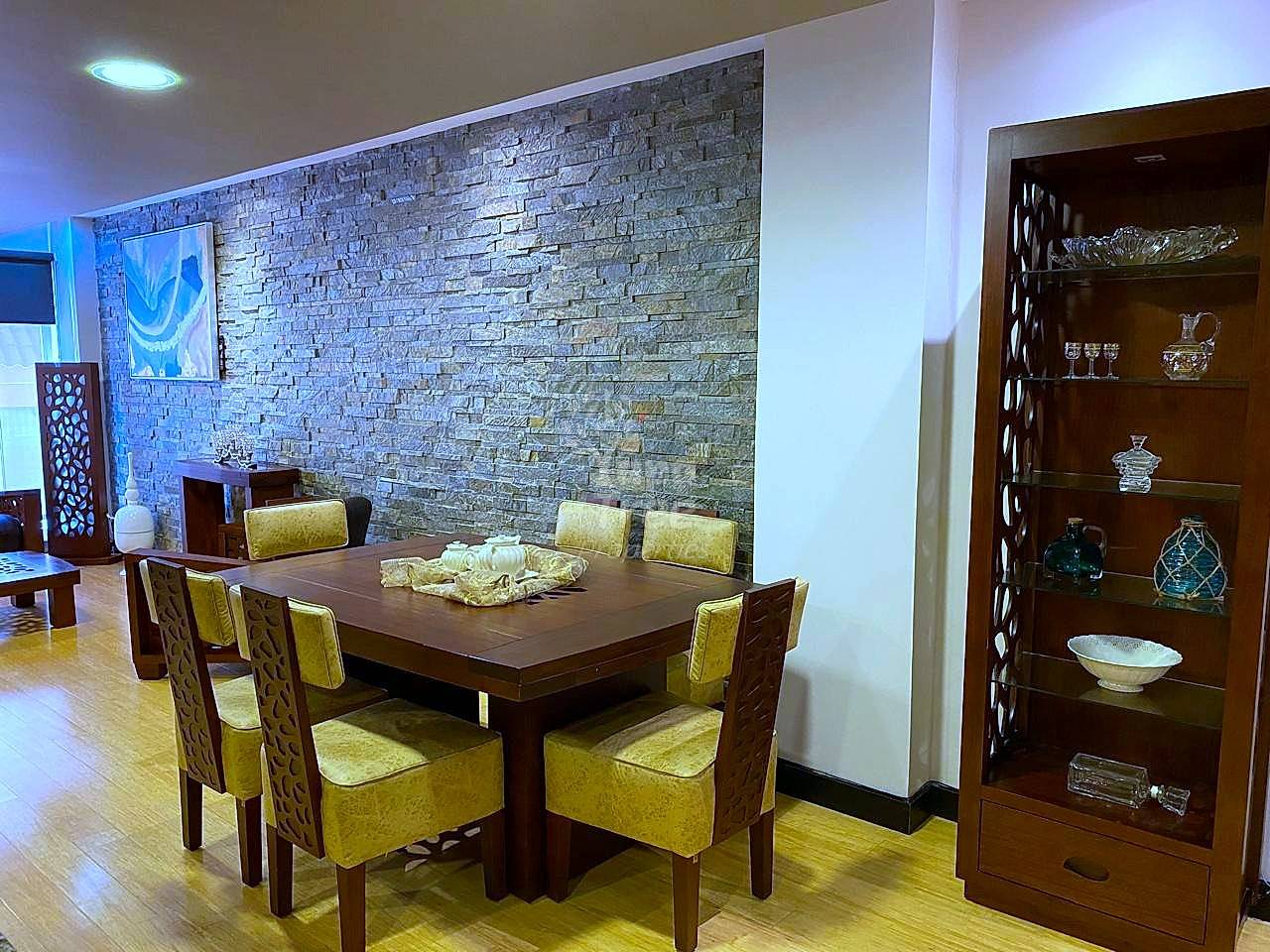 Dining room with dark wood table, six yellow upholstered chairs, stone accent wall, recessed lighting, and dark wood display cabinet with decorative items.
