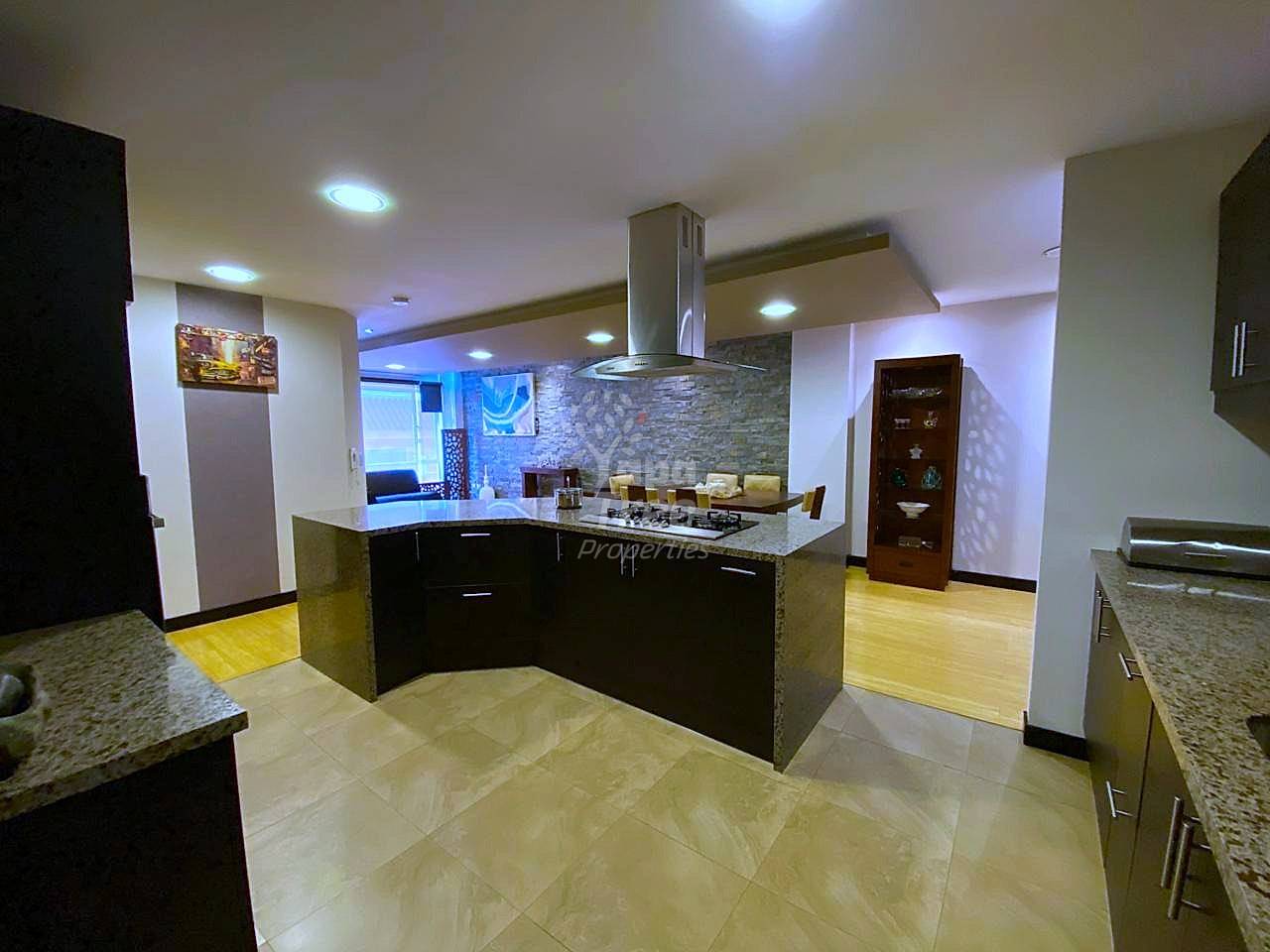 Modern cocina with black cabinetry, gray granite countertops, central island with gas cooktop, stainless steel range hood, and ceramic tile flooring throughout.