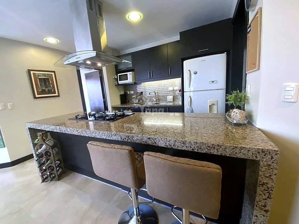 Modern cocina with black cabinets, granite countertop island, two brown bar stools, white refrigerator, gas cooktop, and stainless steel range hood.