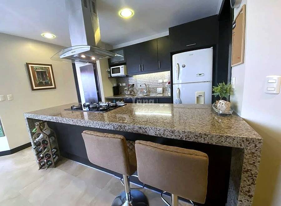 Modern cocina with black cabinets, granite countertop island, two brown bar stools, white refrigerator, gas cooktop, and stainless steel range hood.