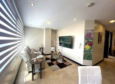 Living room with gray sofa, wall-mounted TV, striped window blinds, recessed ceiling lights, and floral artwork on accent wall