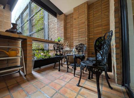 Interior patio with terracotta tile floor, exposed brick walls, black ornate chairs, wooden shelving, and green plant wall visible through metal mesh window.