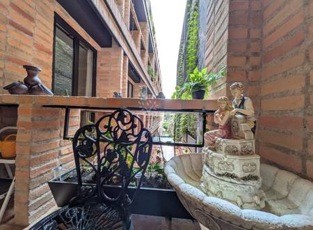 Narrow balcony with exposed red brick walls, black wrought iron railing, decorative statue, and potted plants overlooking adjacent building
