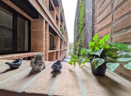 Concrete balcony with potted green plant, decorative ceramic figurines, brick building facade, and ivy-covered walls in background